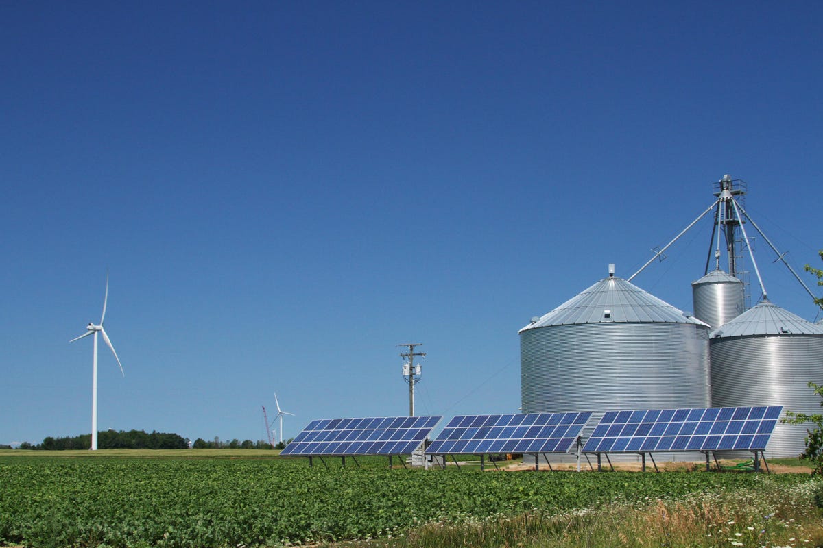 Solar panels, windmills and grain bins against a blue sky