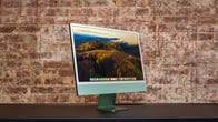 Apple iMac M3 in green on a black desk in front of a brick wall.