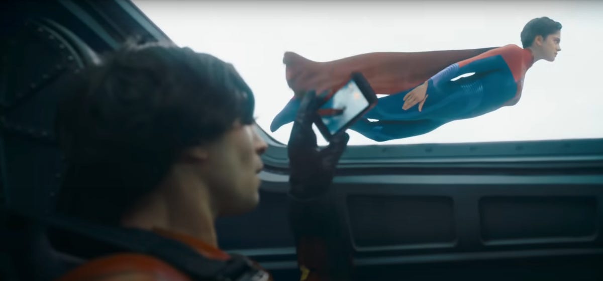 Barry Allen takes a photo of Supergirl on his phone as she flies outside the cockpit of his plane in The Flash.