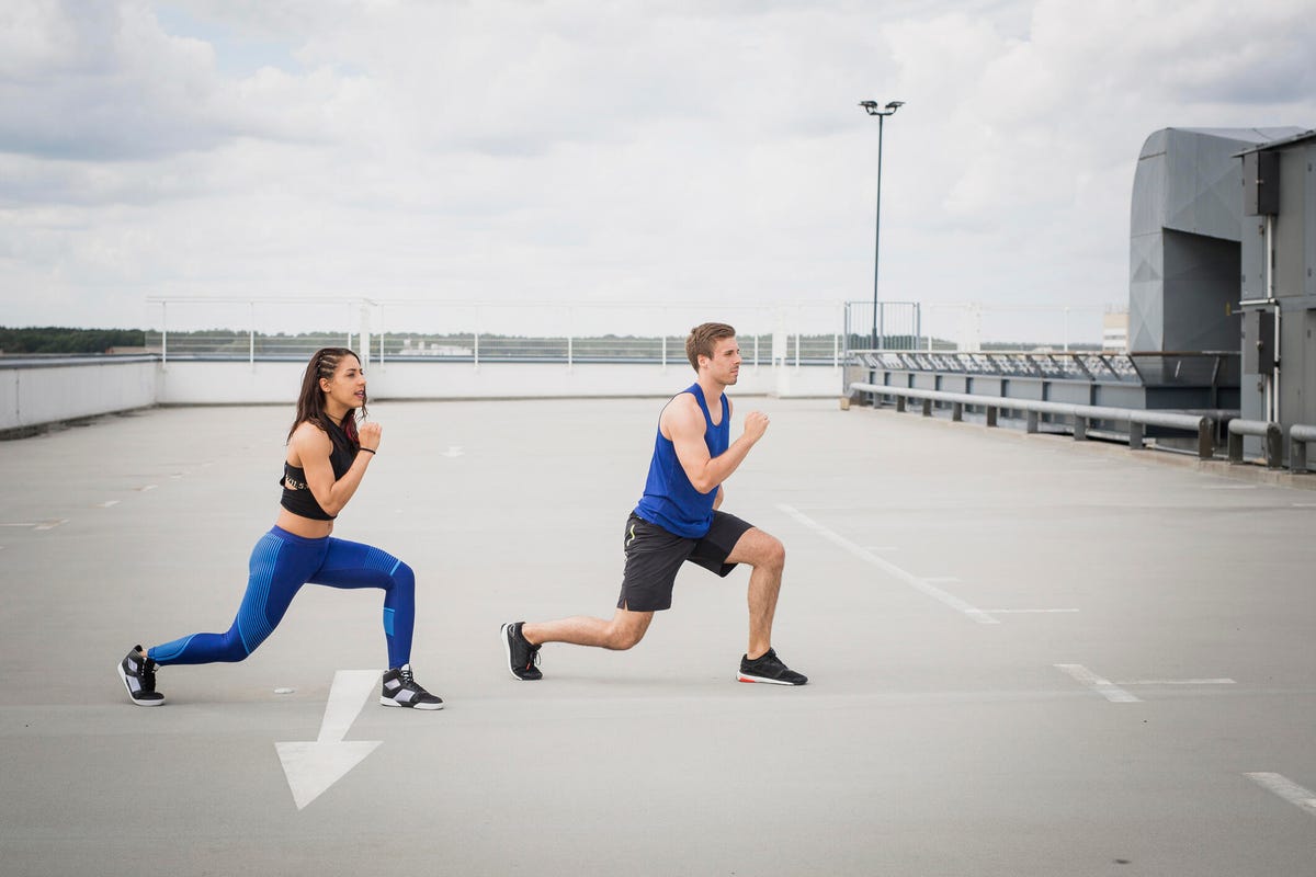 A young woman and man doing lunges on a rooftop parking lot