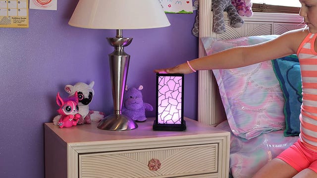 A child touching a friendship lamp on her bedside table so that it lights up.