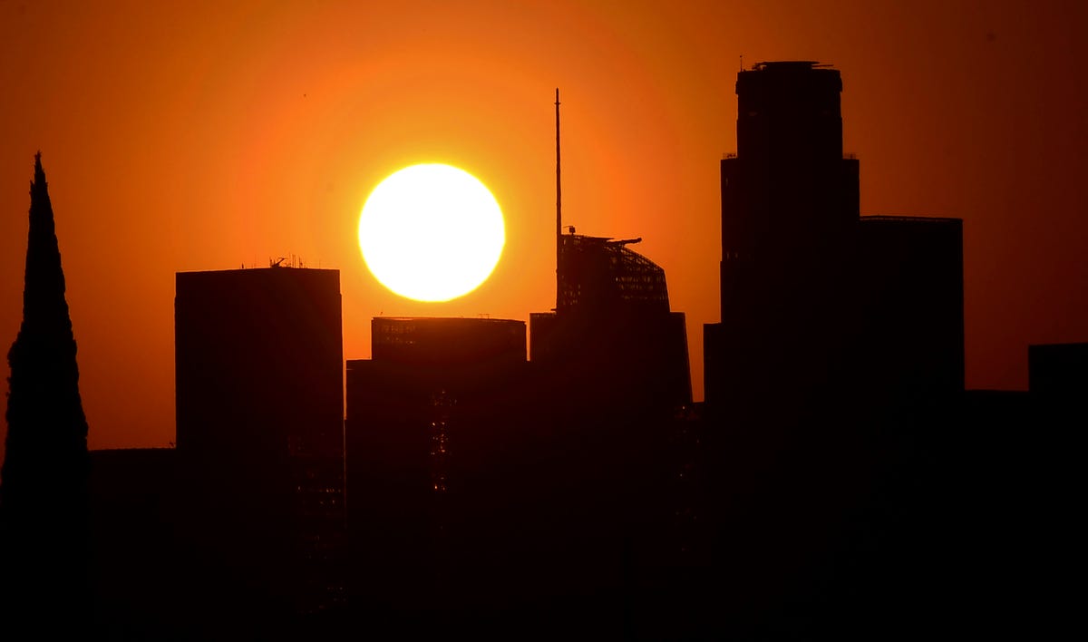 The sun sets behind tall buildings in downtown Los Angeles, California