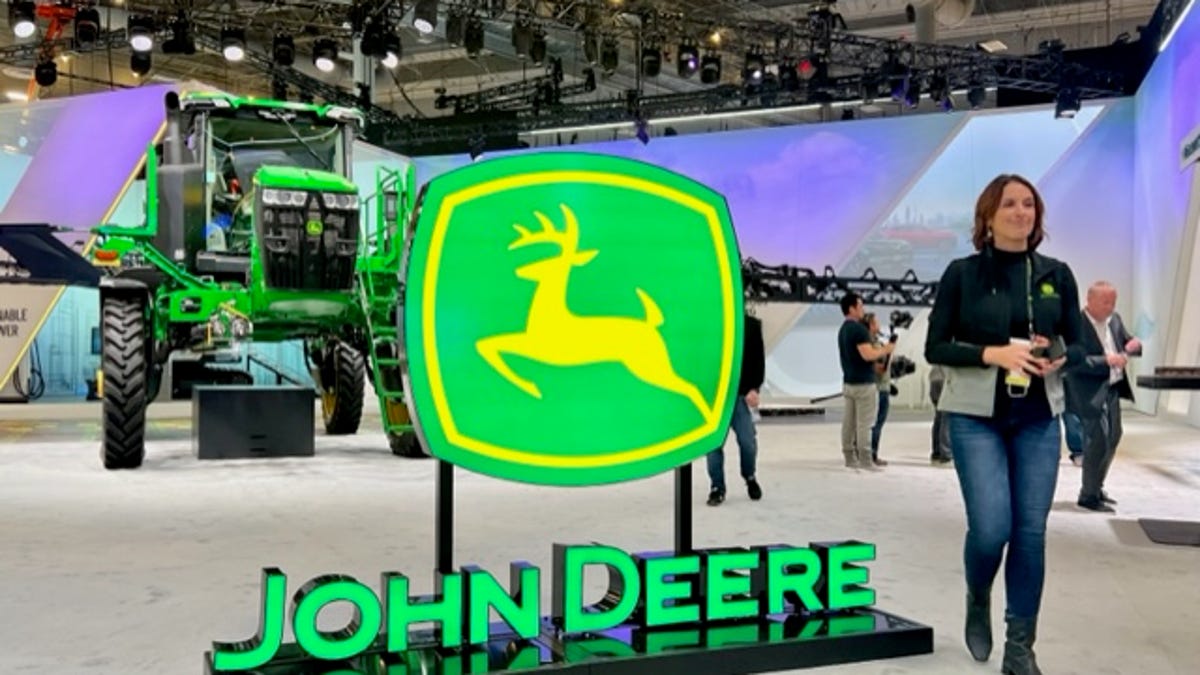 An image of the John Deere logo in front of one of its crop sprayers.