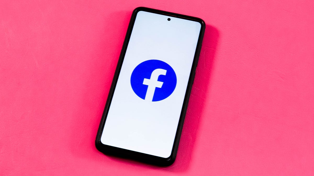 Facebook logo on a phone in front of a pink background.