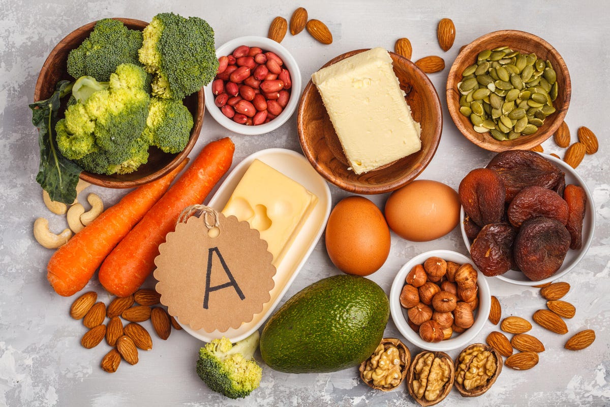 Assortment of high vitamin A foods like carrots, nuts, broccoli, butter, cheese, seeds and eggs.
