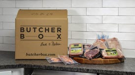 A variety of meats are displayed on a counter next to a delivery box from ButcherBox.