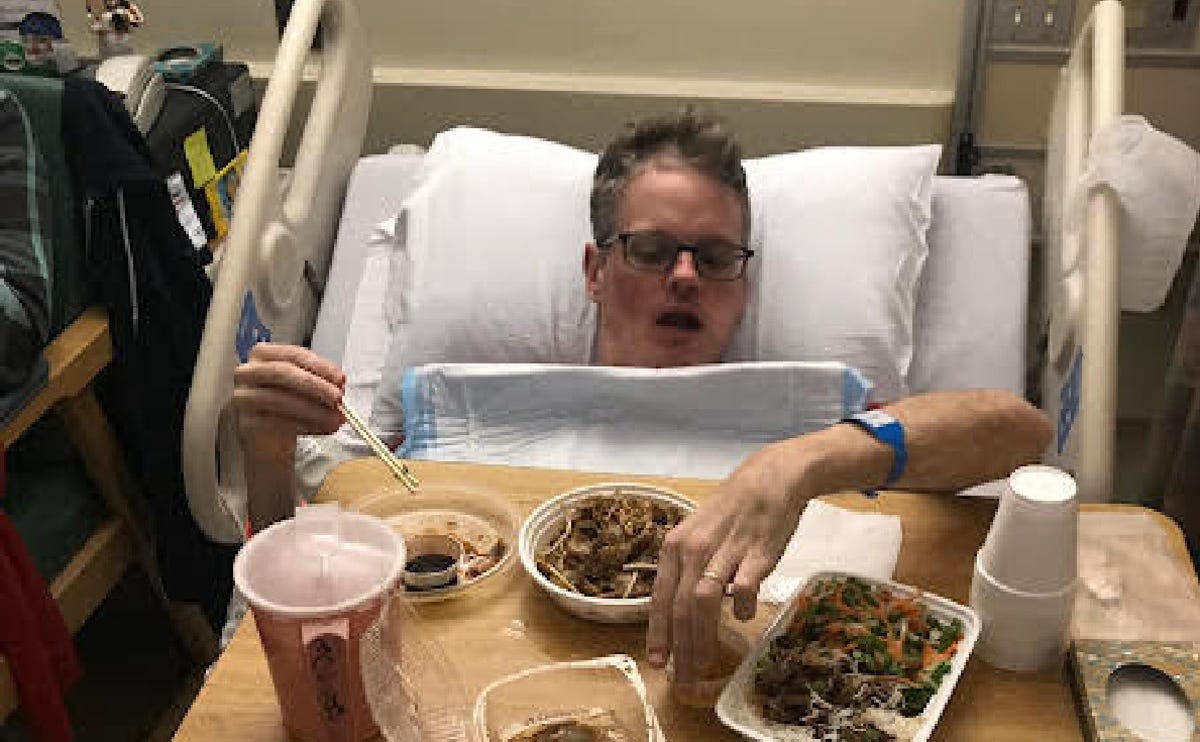 Drew Magary in a hospital bed with food for him to eat