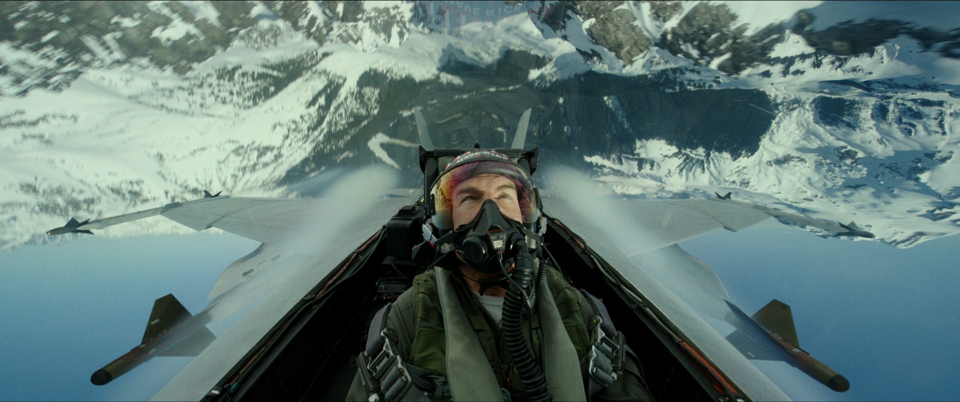 A viewer from the cockpit of a fighter plane flying upside down over mountains in Top Gun: Maverick.