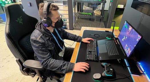A man sits at a computer playing a game, feeling haptic feedback through headphones using Razer's new software developer kit.