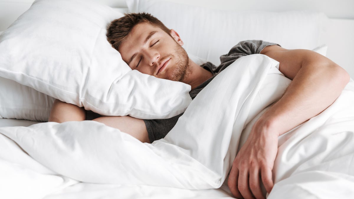 A man taking a nap with a white pillow and comforter
