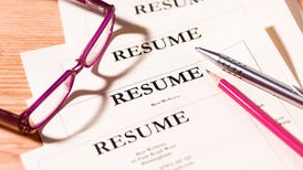 Four resumes on a desk with pens and a pair of glasses