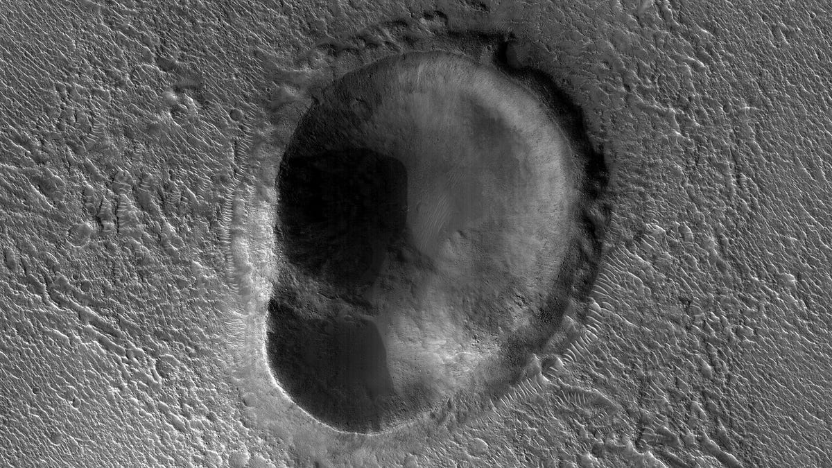 A black and white photo shows a rocky Martian landscape with an ear-shaped crater.