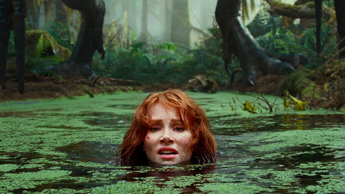 Scared Bryce Dallas Howard sinks into a swamp as a dinosaur follows in Jurassic World: Dominion.