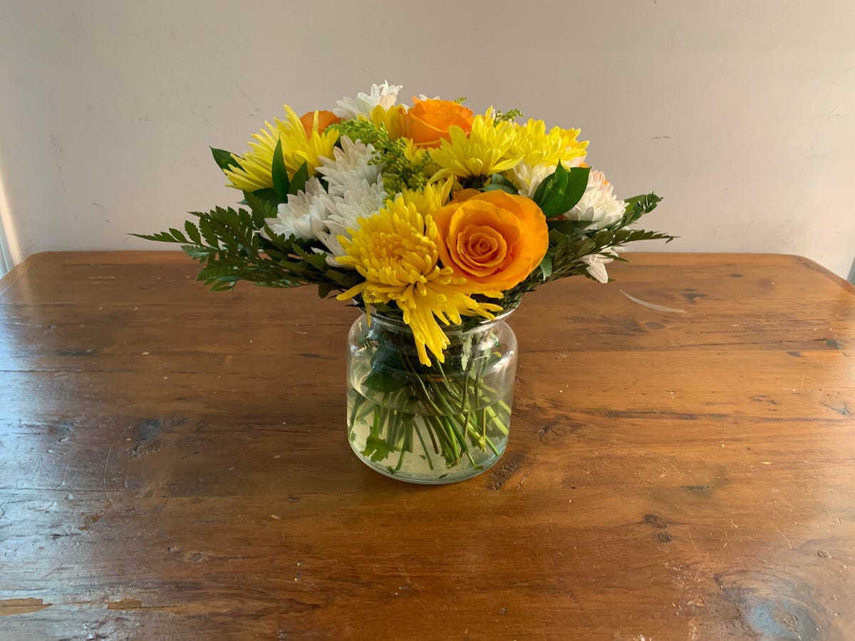 A vase of yellow, orange and white flowers.