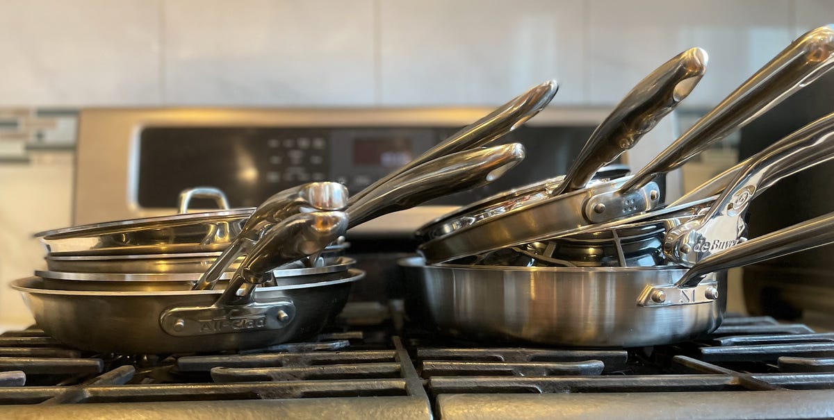 A pile of pans stacked on top of each other rest on a stovetop range.