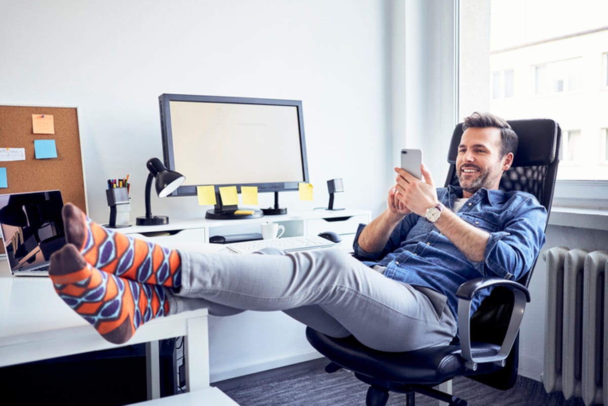 Man relaxing in his desk chair with his legs propped up and his phone in his hand.