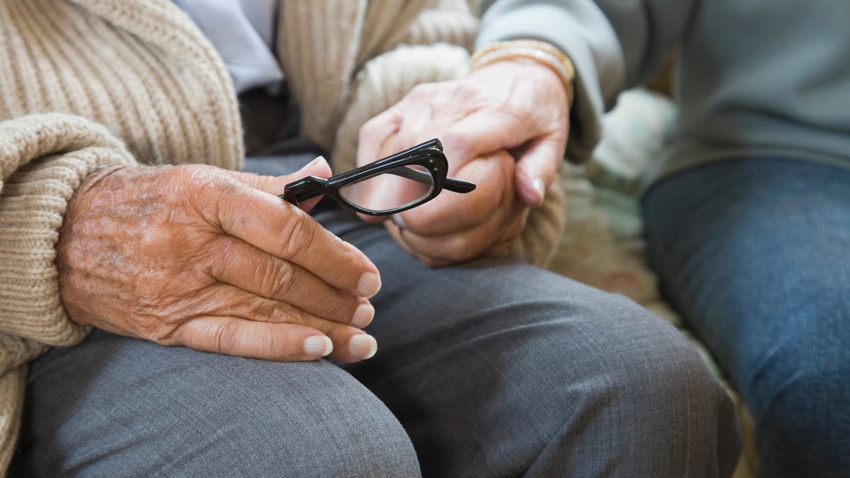 A senior couple holds hands, with one of them holding a pair of reading glasses