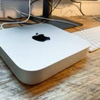M1 Mac Mini on a wooden desk next to an Apple keyboard