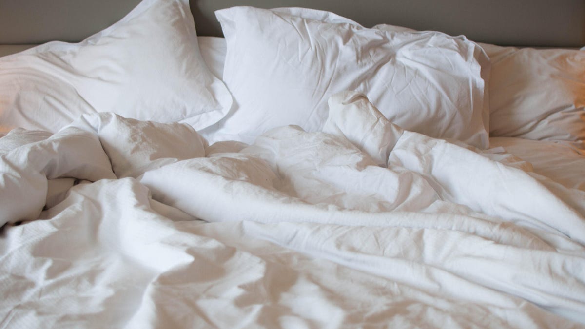 An unmade bed with white sheets and pillows