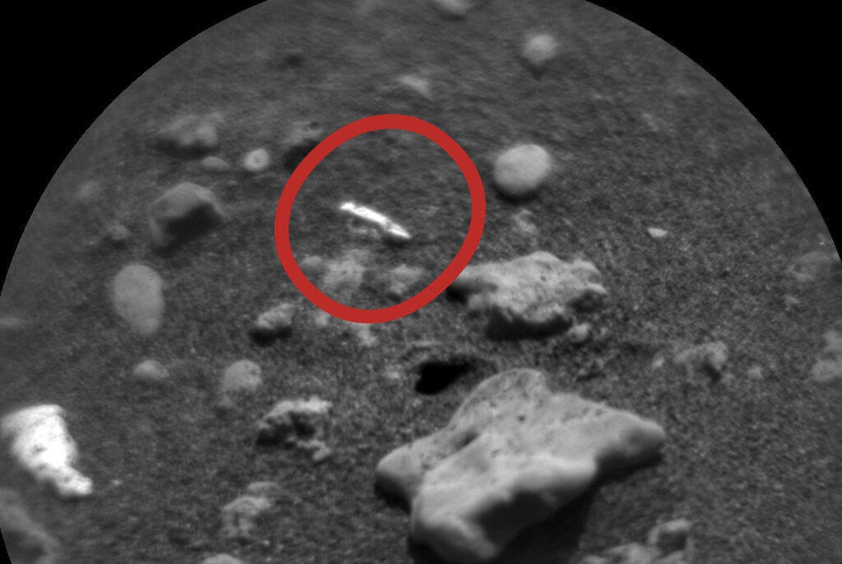 A red circle highlights a small drill-bit-shaped rock in a black and white closeup of Mars surface.