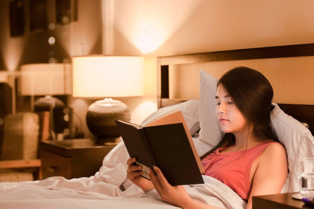 Young woman lying in bed reading a book