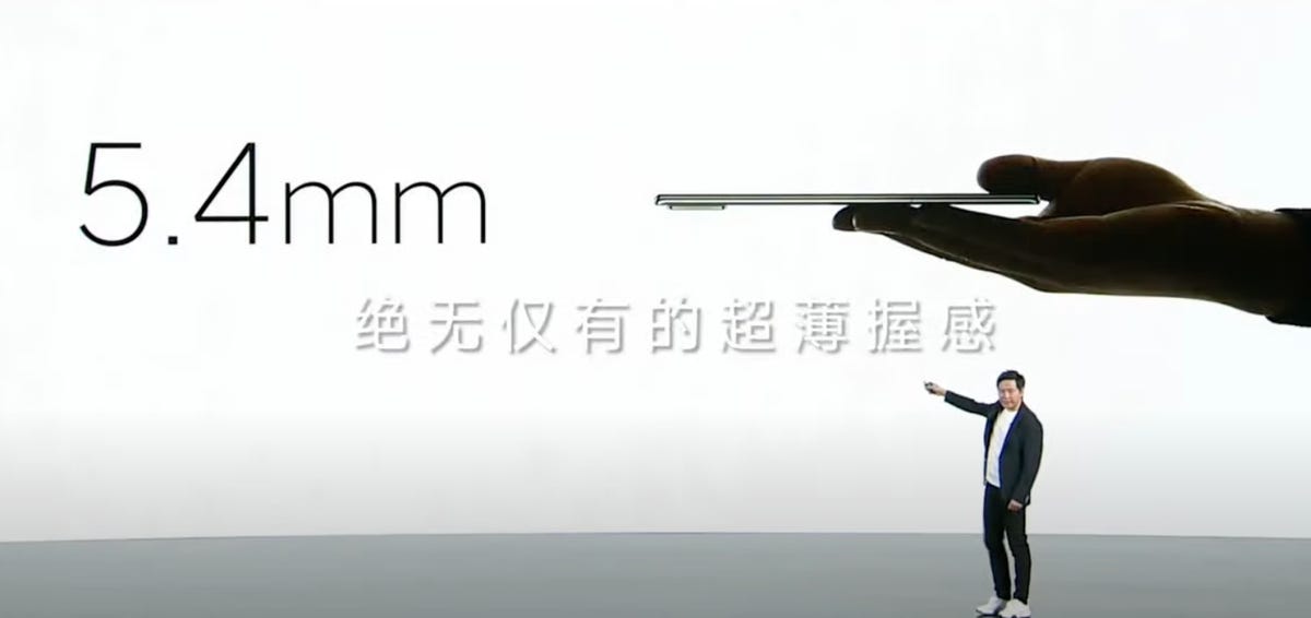 Xiaomi CEO Lei Jun on stage pointing to a slide with a hand in silhouette holding a phone sideways and the figures 5.4mm