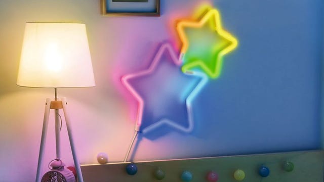 Neon Rope lights from the GE Lighting Cync lineup are flexed into the shape of two stars on a bedroom wall, and shining out a rainbow of multi-colored light.