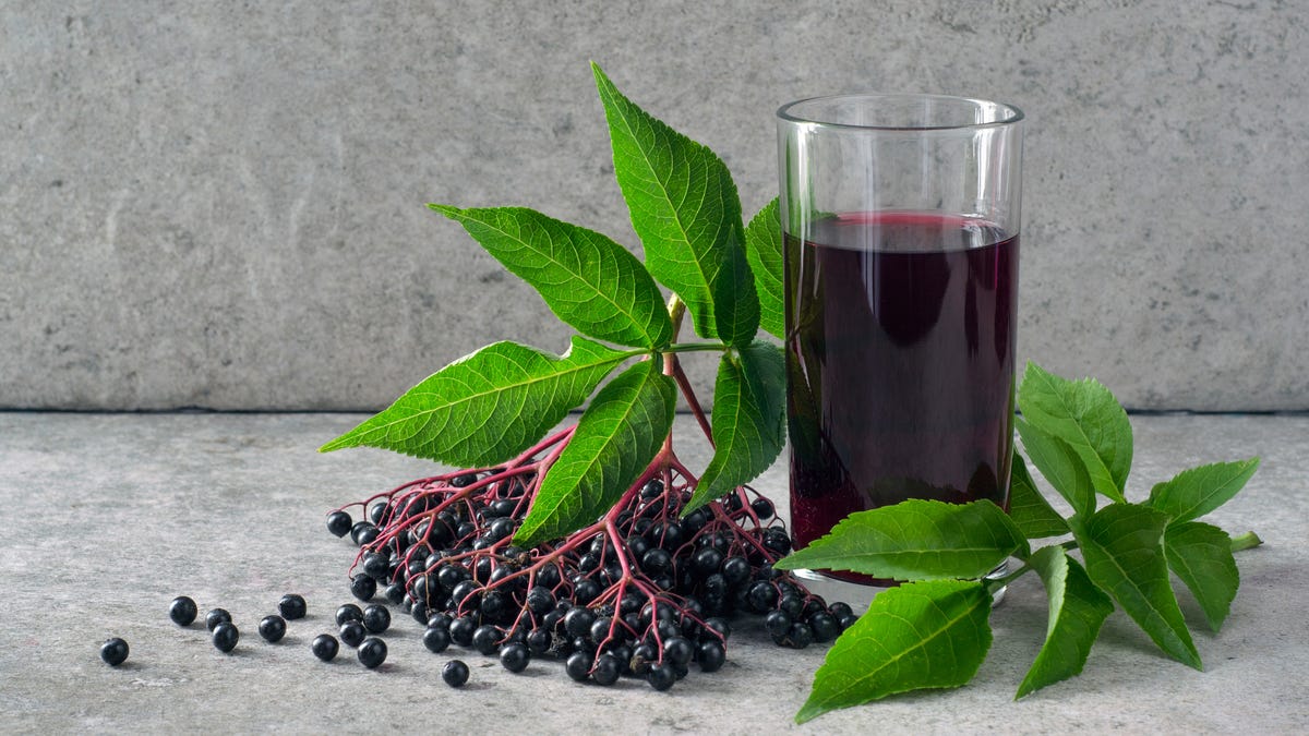 A branch of elderberry next to a glass of elderberry syrup