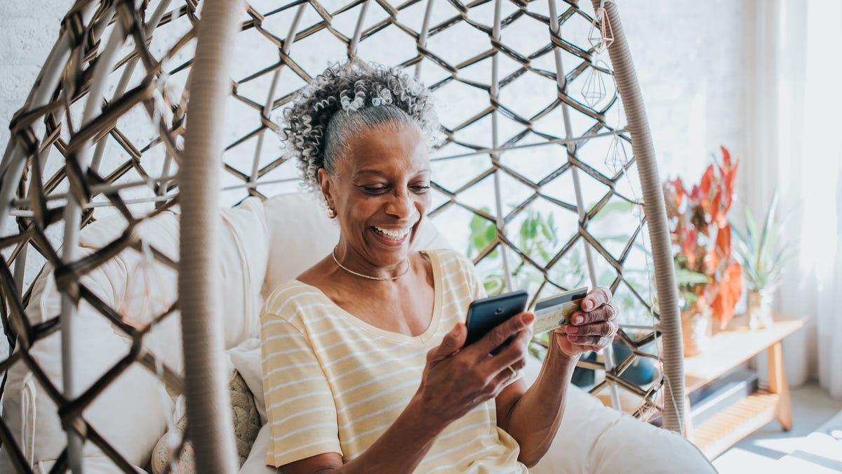 A senior woman using her credit card while holding her cell phone in the living room of a house