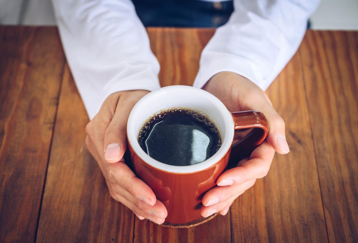 aerial view of a person holding a cup of black coffee with both hands