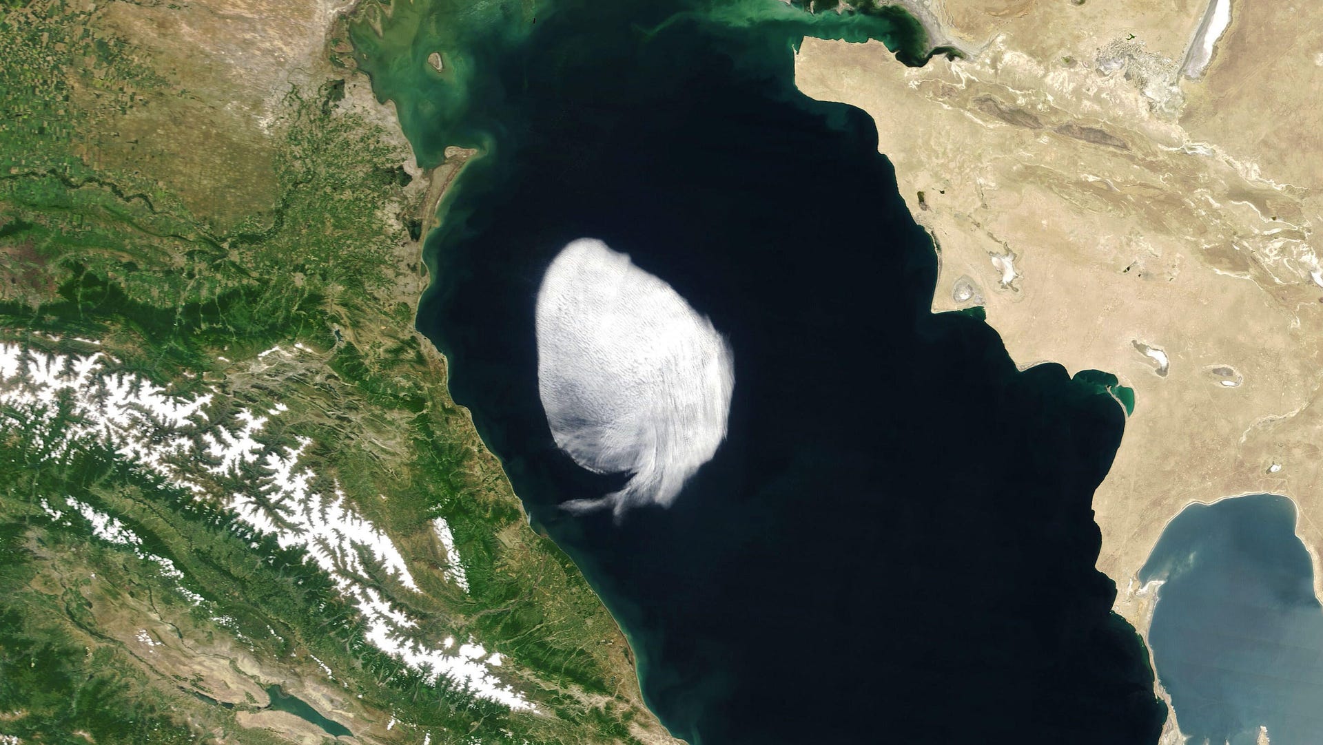 A white oval-ish cloud with definied edges floats above a dark-blue sea with green land to the left and desert land to the right.