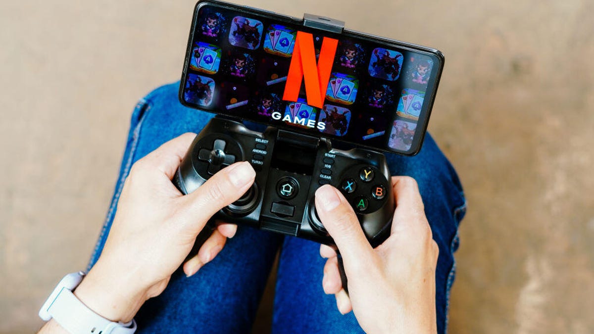 A person holding a smartphone with the Netflix logo on it. The smartphone is attached to a gaming controller.