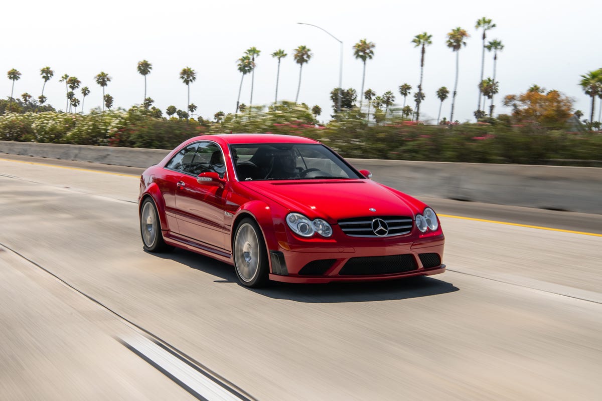 Front 3/4 view of a red Mercedes-Benz CLK63 AMG Black Series on a highway, flanked by palm trees