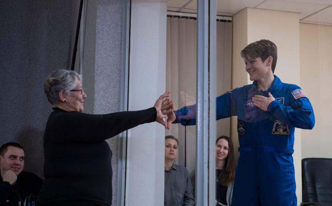 L'astronaute Anne McClain tient une main sur son cœur tout en touchant la main de sa mère avec l'autre à travers une vitre