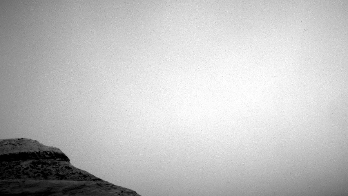 A small hill-like formation projects against a blank-looking sky on Mars.