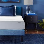 A white AmazonBasics mattress on top of a blue bed frame with blue accent pillows on top. 