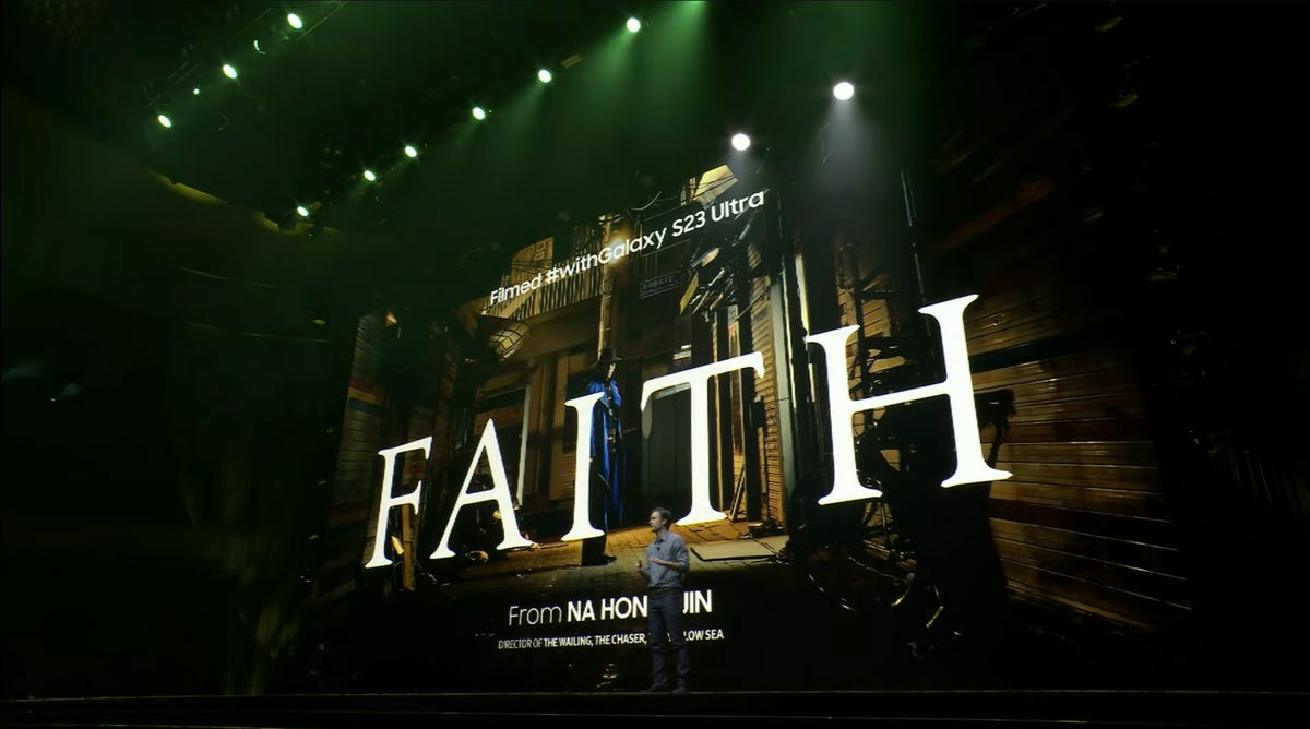 The Samsung Unpacked stage is filled with a giant digital poster for Hong-jin's short film Faith, which shows an ominous man in a broad-brimmed hat, painted face and starkly blue jacket standing in a dimly-lit alley.
