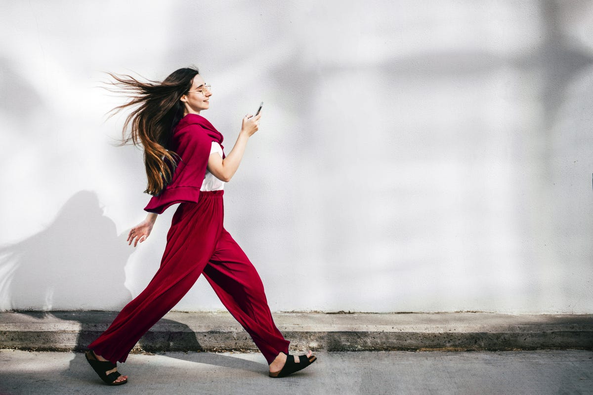 A woman in a red sweat suit walks briskly with her phone in her hand