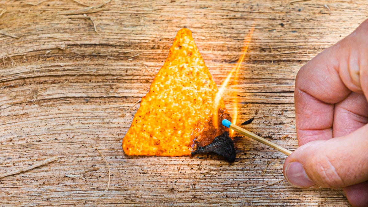 A single Doritos chip is light on fire with a match