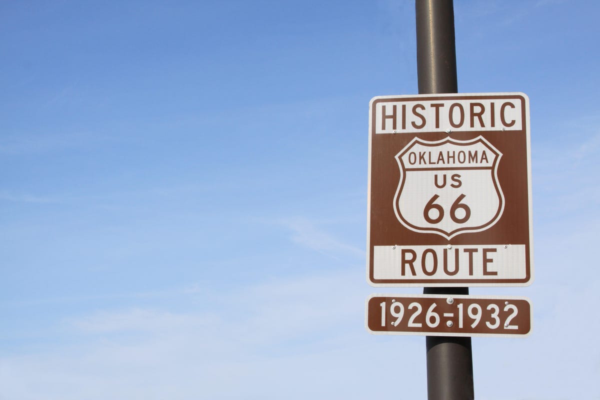 A highway sign is photographed against a blue sky along old Route 66 in Oklahoma.