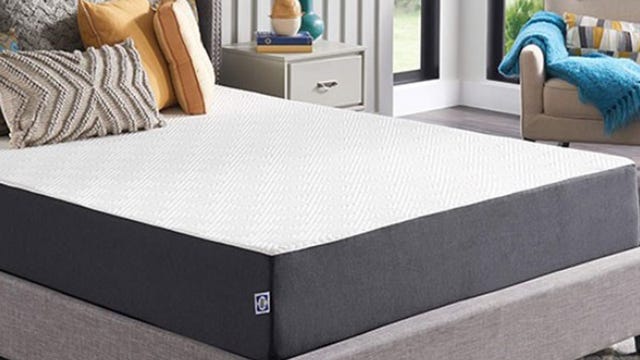 A Sealy mattress sits on a bedframe near a nightstand and chair.