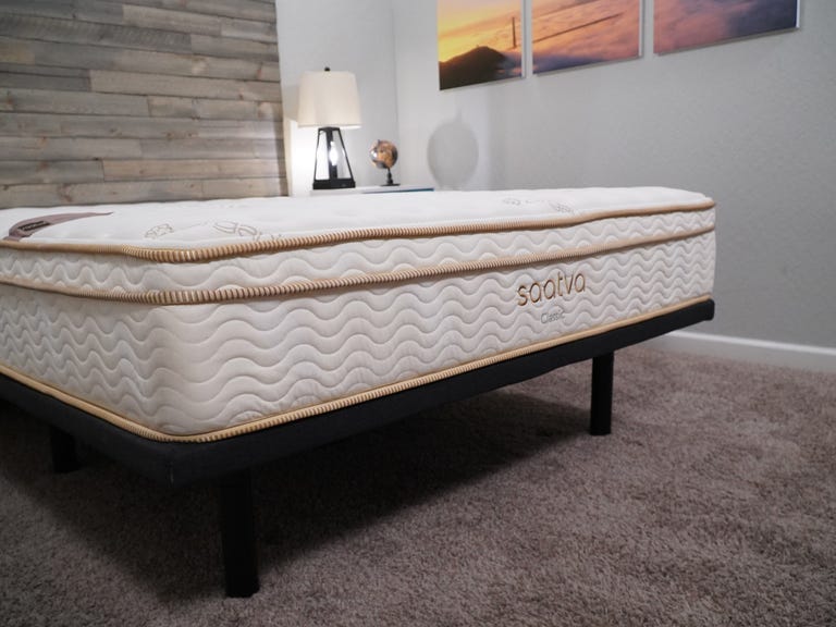 The saatva mattress in a brightly lit room on top of a black bed frame. 