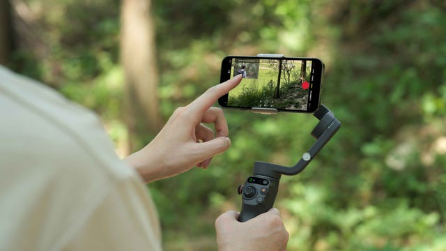 DJI Osmo Mobile 6 camera phone stabilizer being used handheld with a finger tapping on the phone screen.