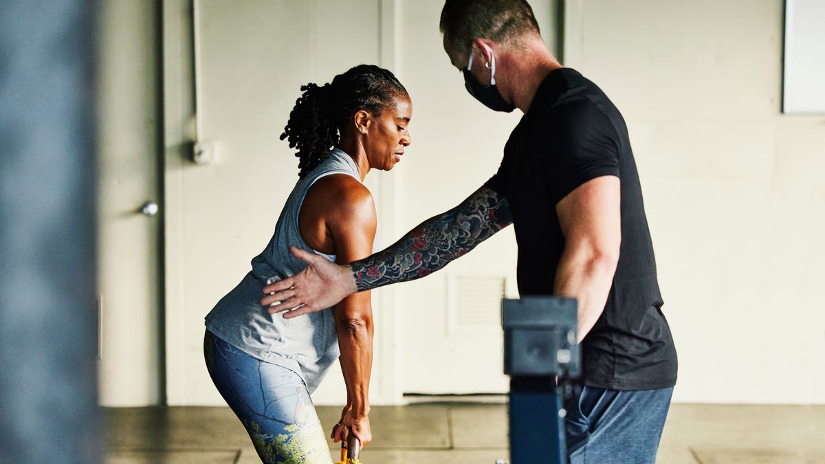 Gym trainer helps guide a client who's lifting a kettlebell.