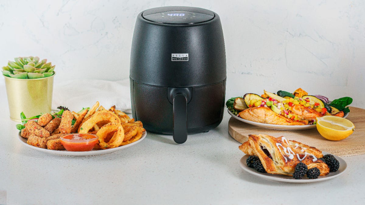 The Bella 2-quart air fryer surrounded by plates of food.