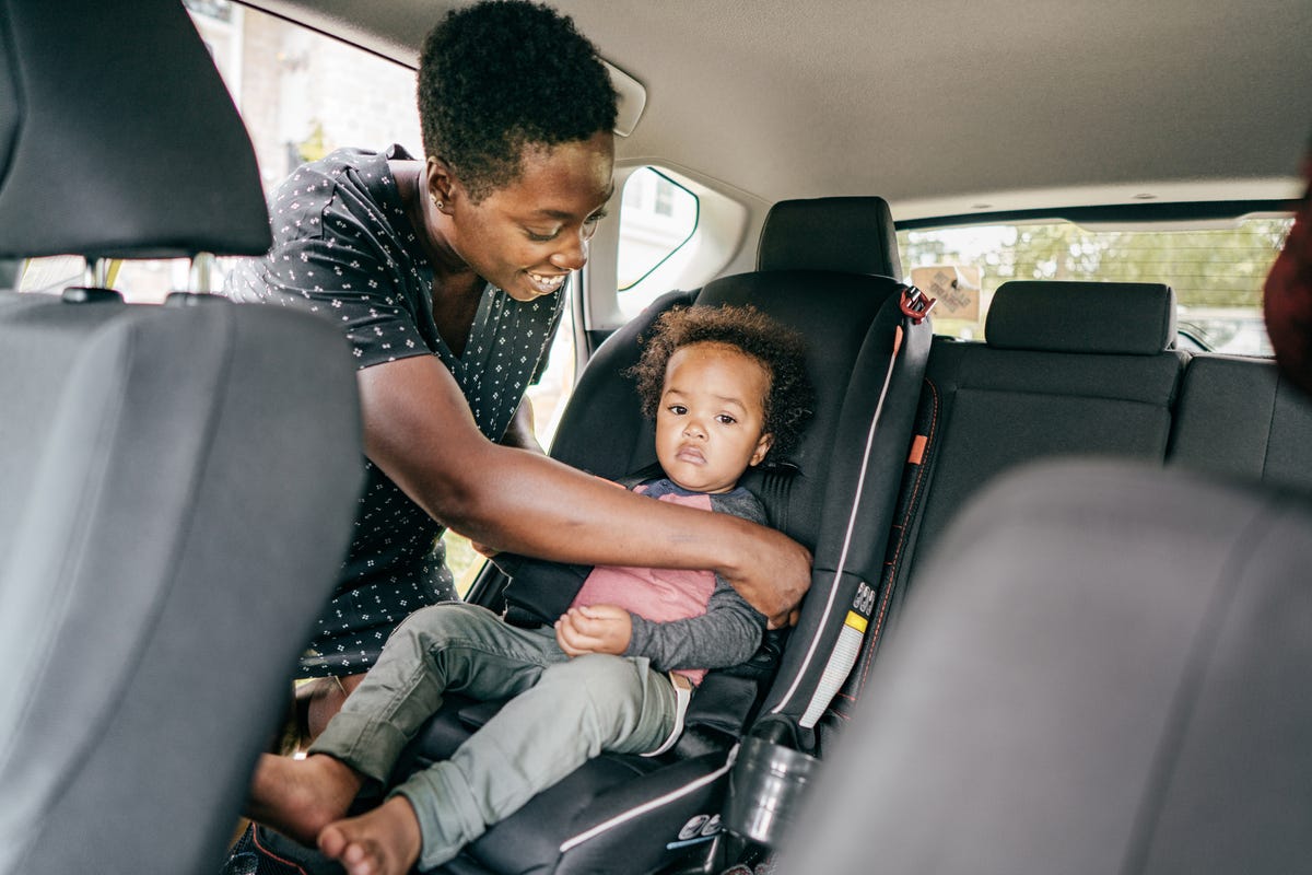 parent straps a child into a front-facing car seat