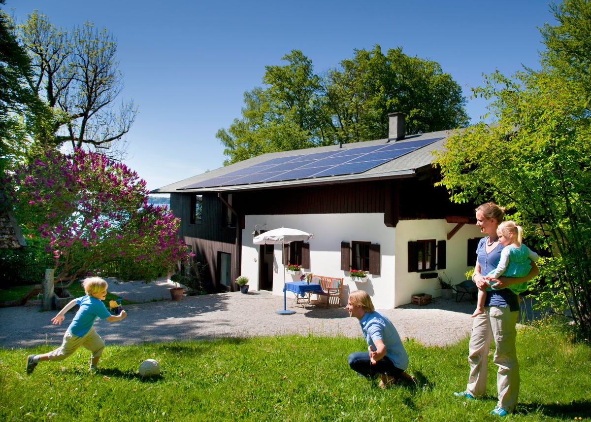 Adults and children on the lawn in front of a home with solar panels.