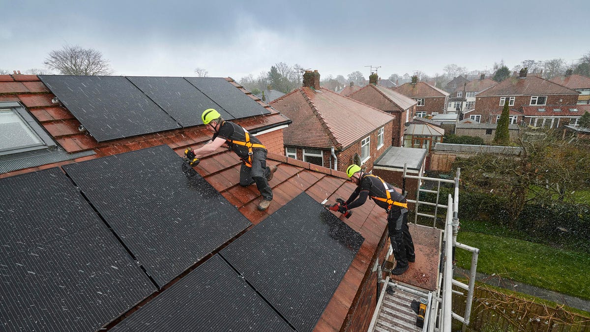 Two people in hard hats installing solar panels on the roof in the rain.