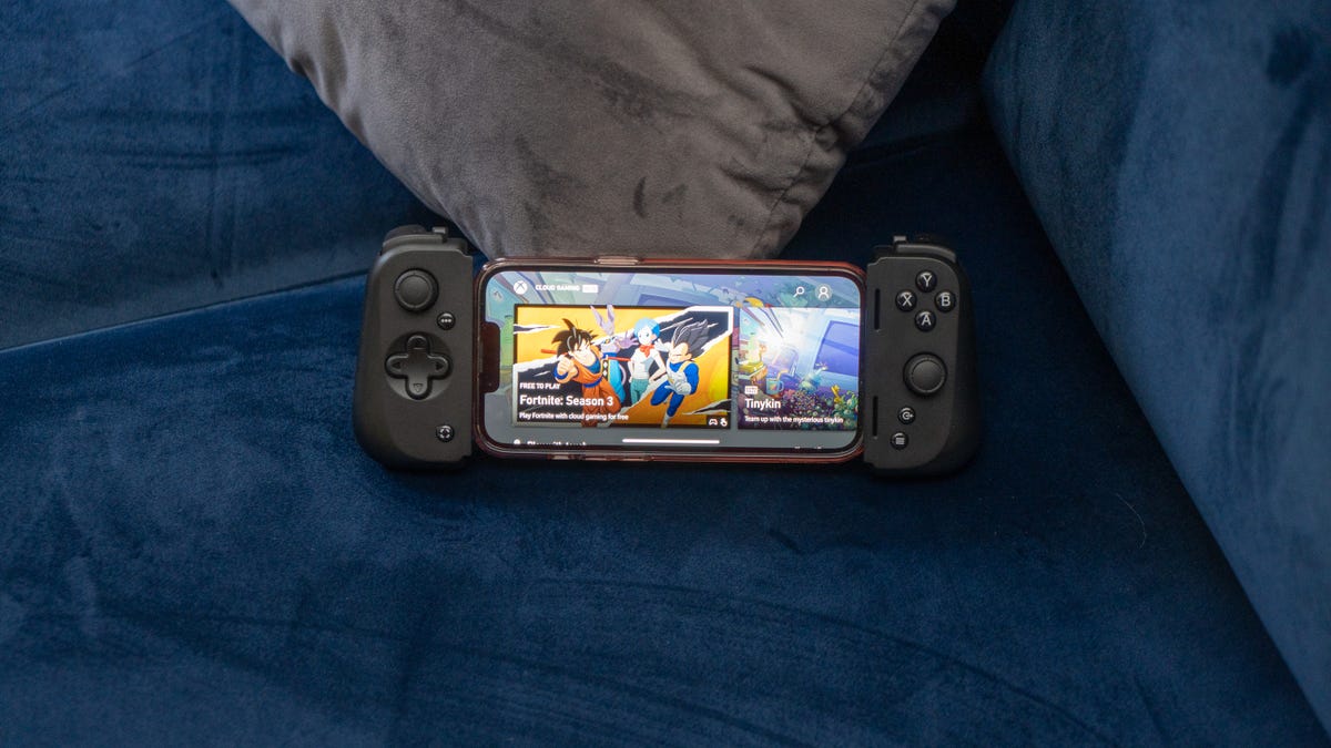 Razer Kishi V2 with an iPhone 13 Pro showing an XBox Cloud Gaming home screen with a large Fortnite thumbnail leaning against a gray pillow on a blue couch