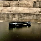 The ThruNite Archer 2A V3 flashlight sits on a black tabletop in front of a wooden wall.
